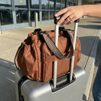 Plexiana bag sitting secured over a suitcase trolley handle outside an airport